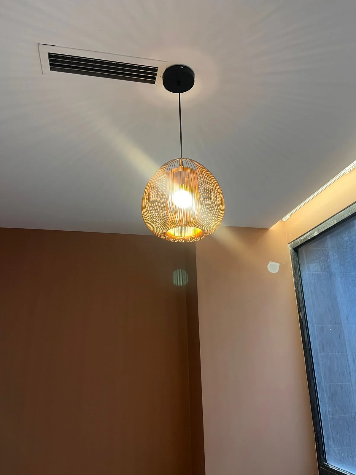 Decorative pendant light fixture hanging from a gypsum ceiling, casting warm light in a living room